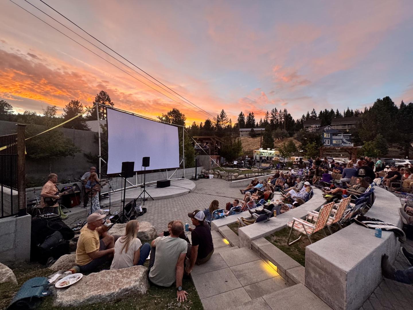 Outdoor crowd watching a film on a large screen at sunset.