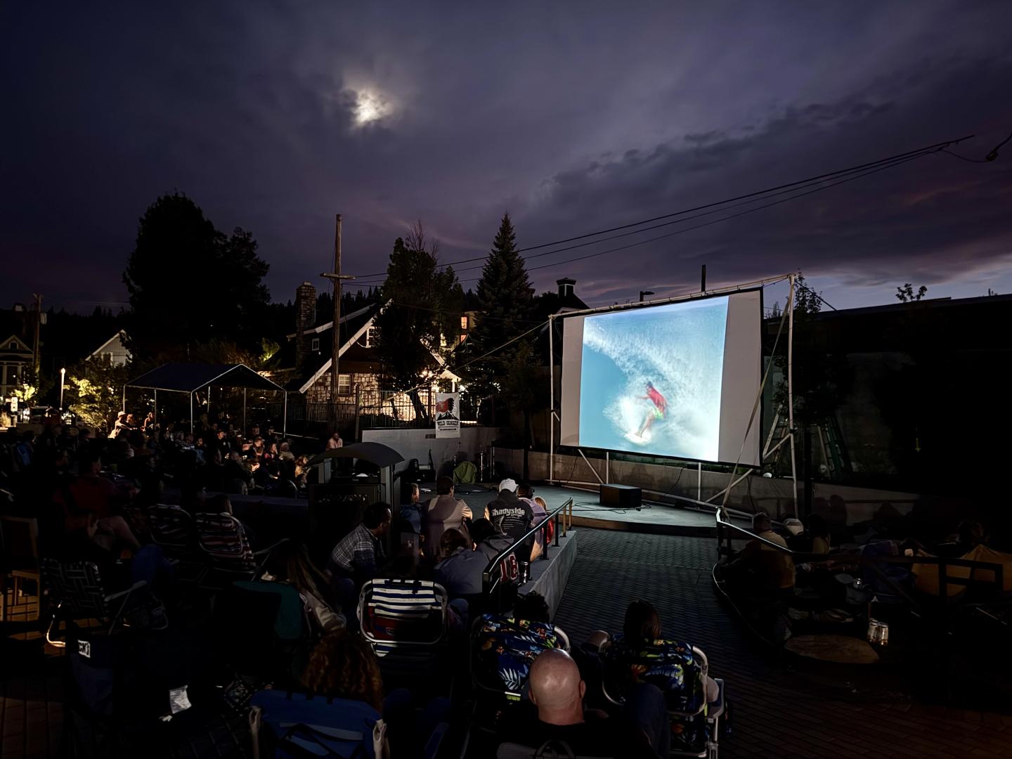 Outdoor nighttime movie screening with audience seated before a glowing projection screen.