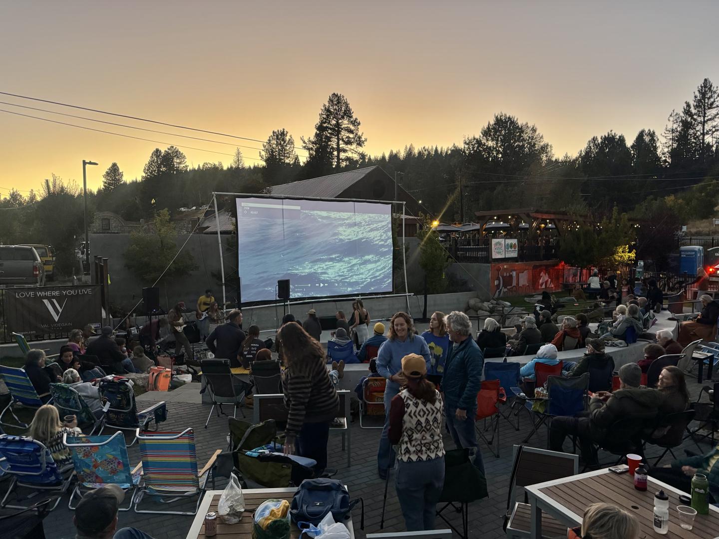 Outdoor crowd watching a film on a large screen at sunset.