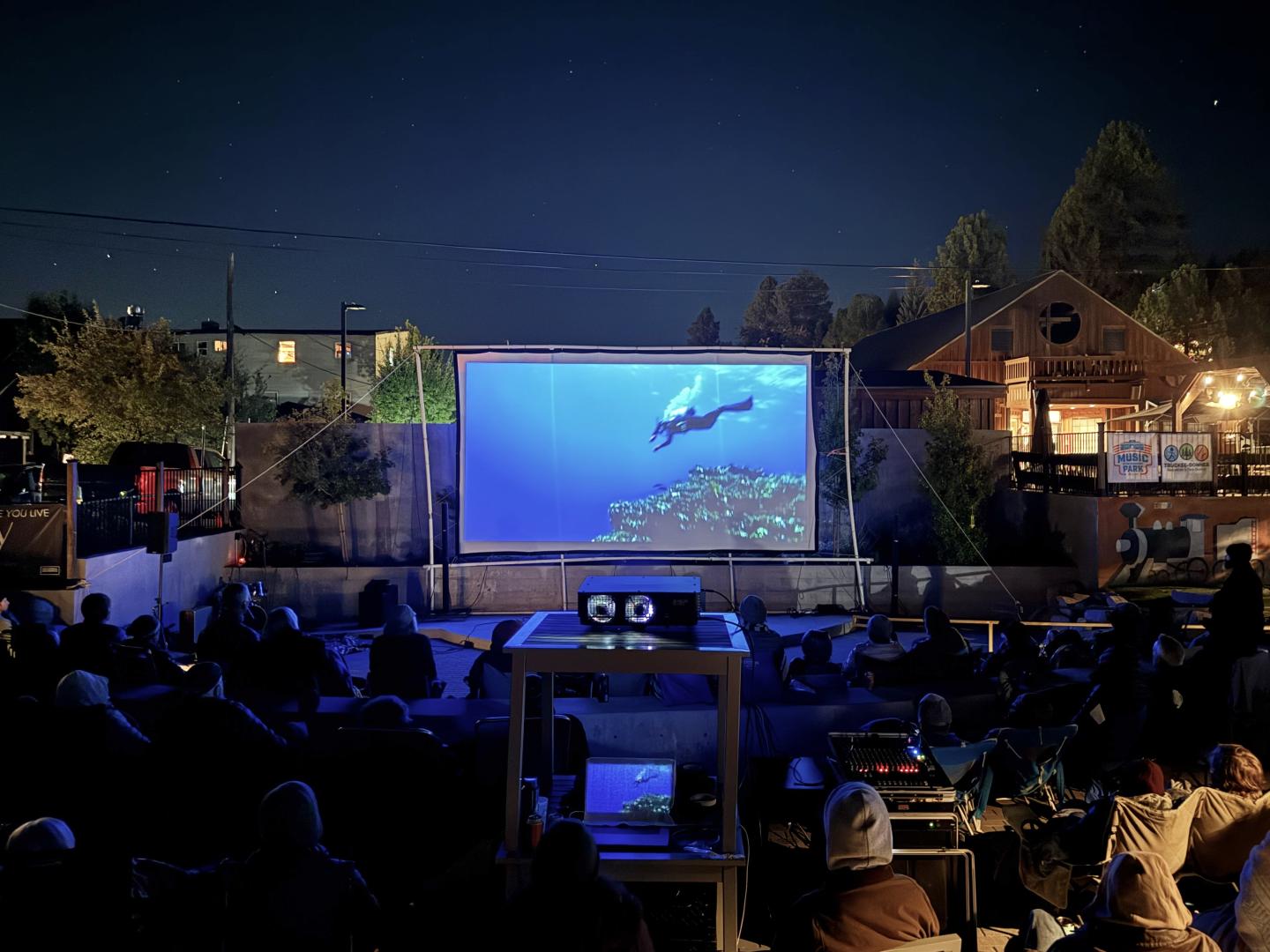 Outdoor nighttime concert with audience watching a blue-lit stage screen.