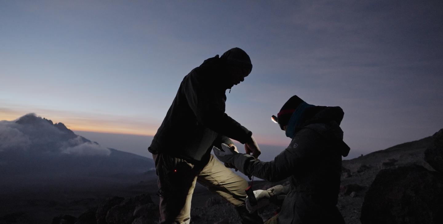 Silhouetted hikers adjusting gear at dusk on a mountain ridge.