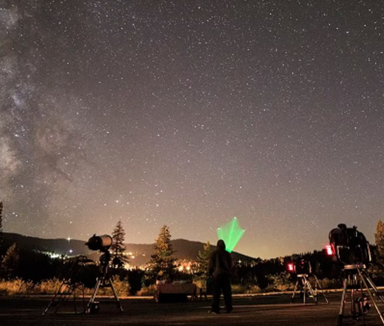 People stargazing beneath the Milky Way, with a green light illuminating one person.