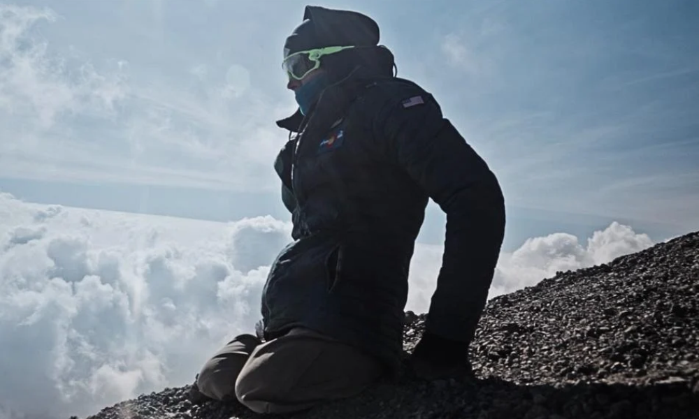 Mountaineer in dark gear sitting on a rocky summit above clouds