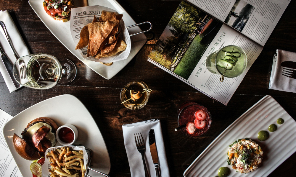 Overhead view of a dark table with plated gourmet dishes and drinks.