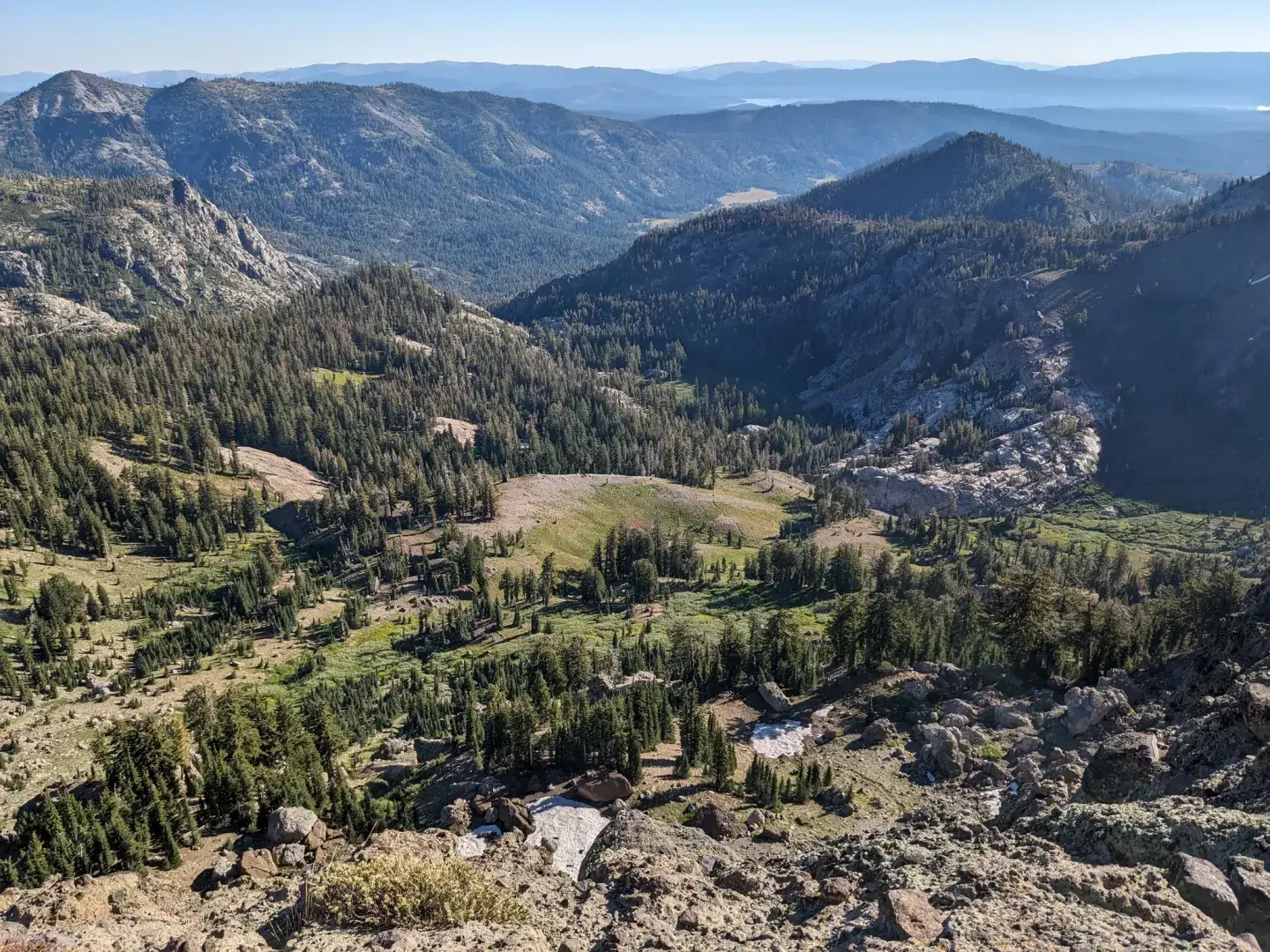 Rocky mountain valley with pine forests, meadows, and distant blue ridges.