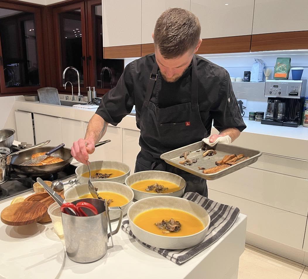 Chef plating bowls of soup in a modern kitchen.