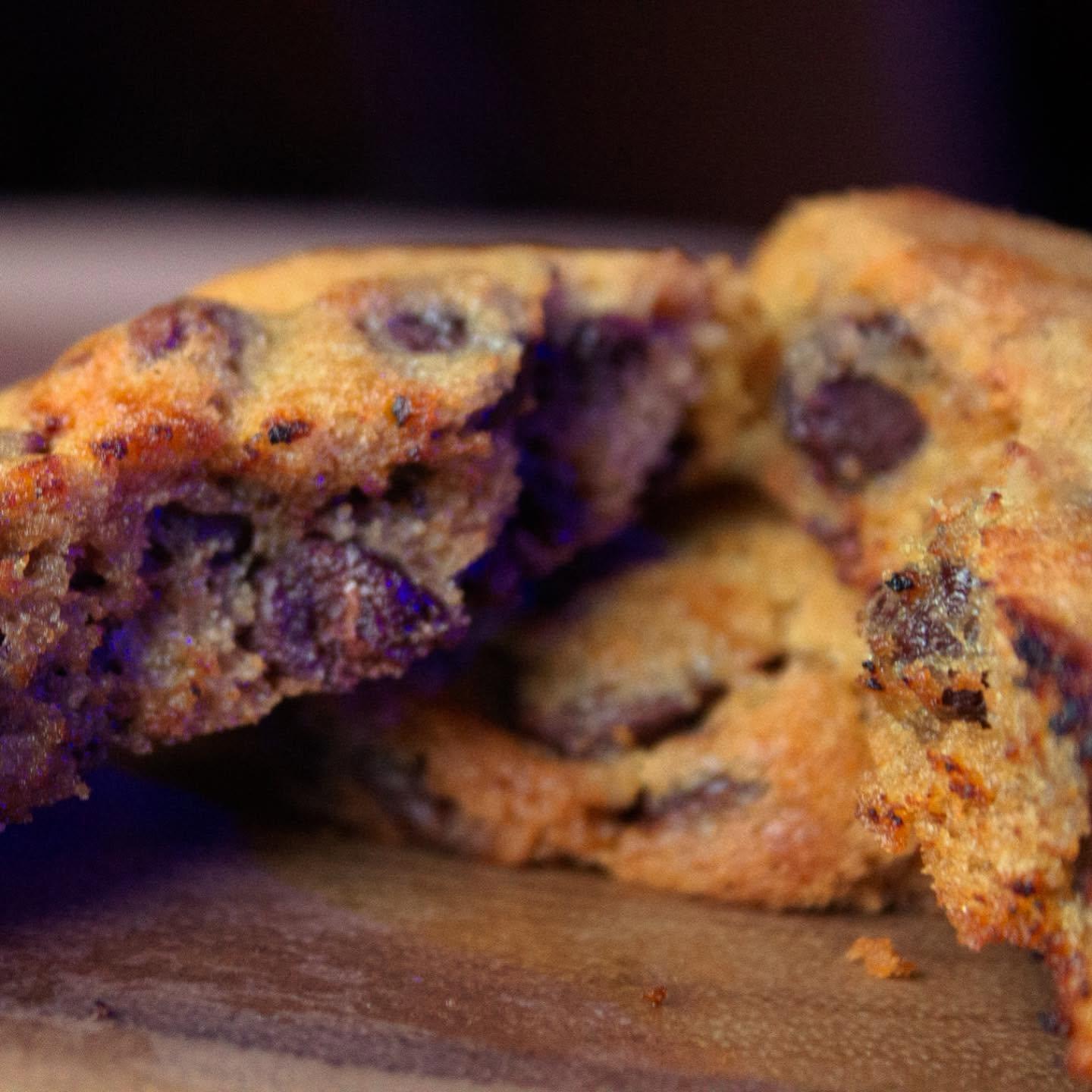 Close-up of warm chocolate chip cookies, one broken open on a wooden board.