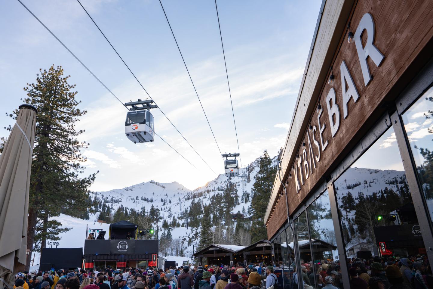 Crowd beneath gondola lifts outside the Lumberbar at dusk.