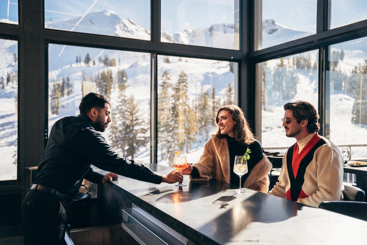 Three coworkers shake hands across a table in a snowy mountain cabin office.
