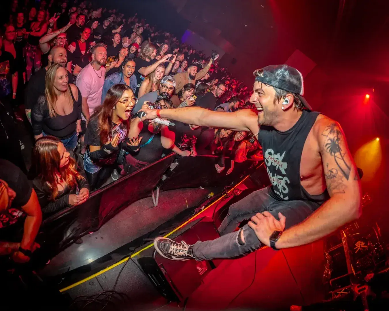 Tattooed singer performs energetically at the stage edge before a cheering crowd.