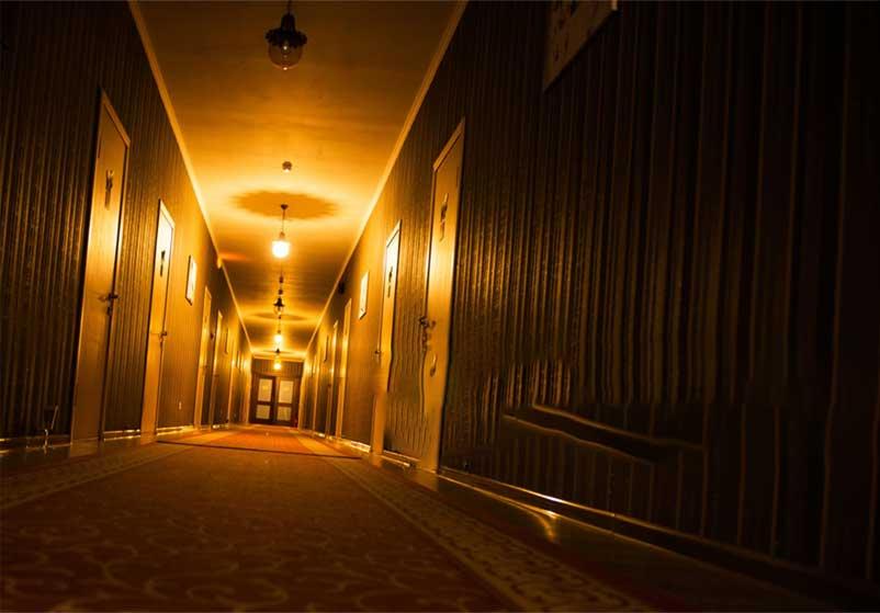 Dimly lit hotel hallway with warm yellow lights and closed doors.