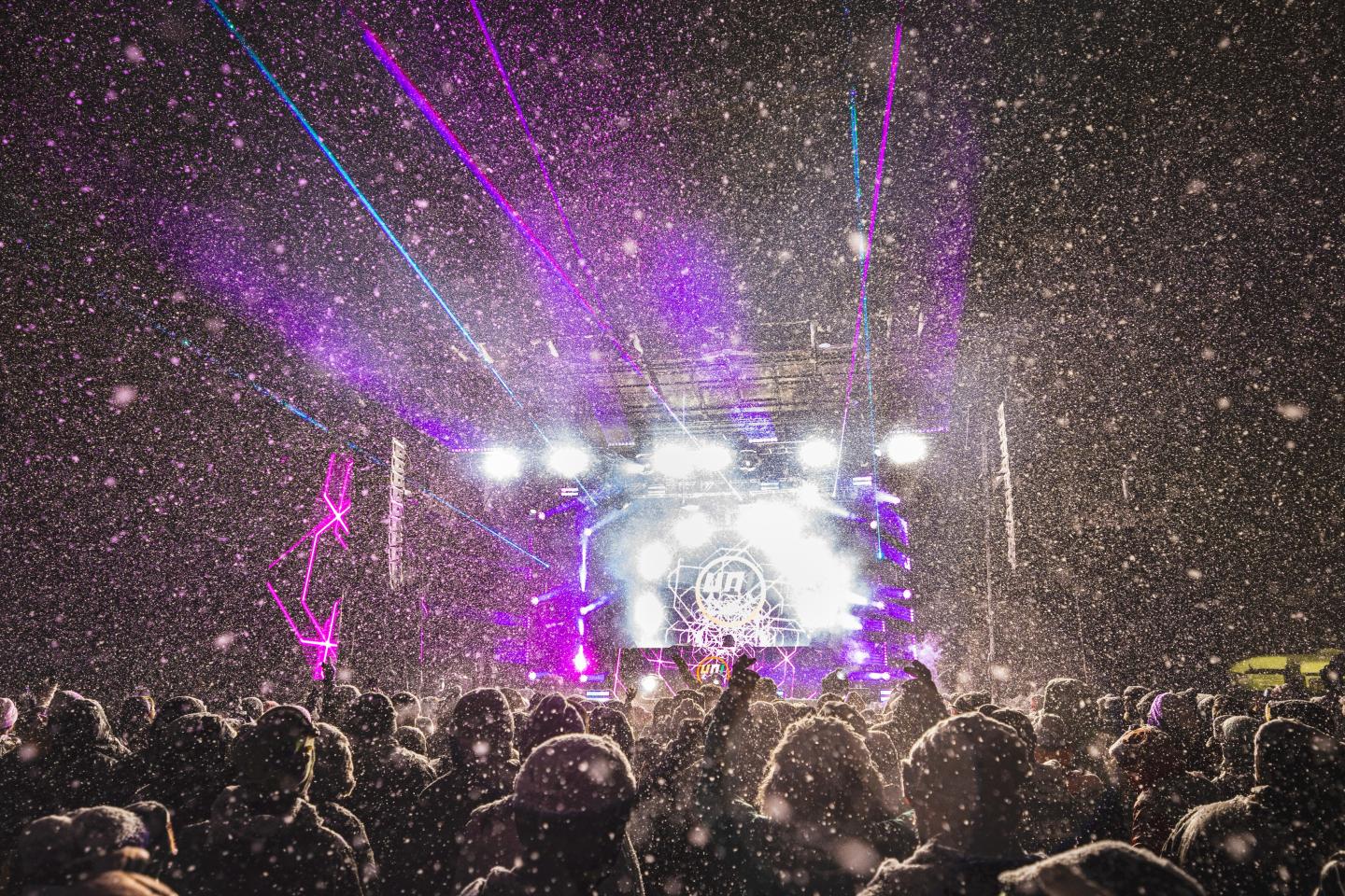 Crowd at a nighttime concert with purple lasers and bright stage lights.