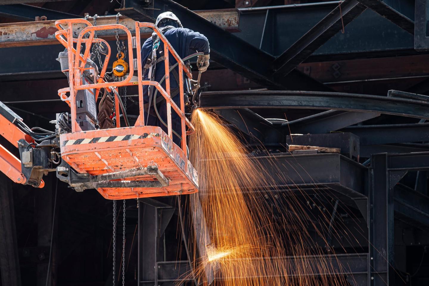 Worker in a lift sprays sparks from a steel mill furnace.