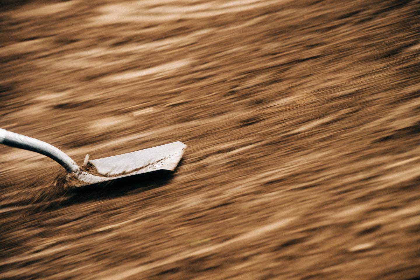 A shovel blade scrapes across blurred brown dirt.