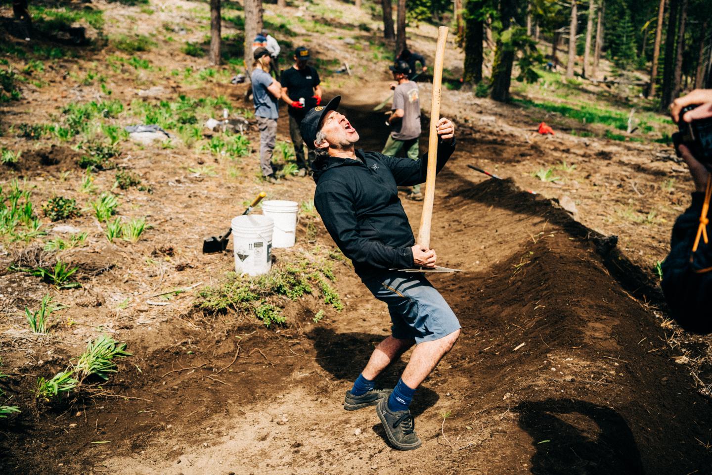 Person in black clothing swinging on a rope over a dirt trench in a forest.
