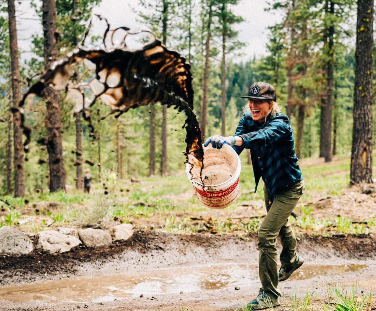 Man tossing a large fish into a basket beside a forest stream