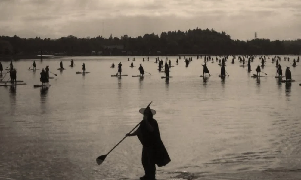 Silhouetted fisher wades through shallow water at dusk, carrying a net.