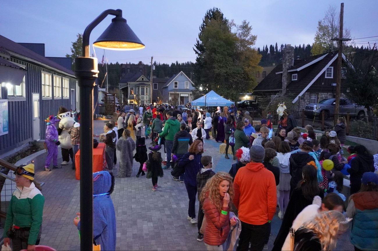 Crowd gathering at an outdoor evening festival beside market tents and buildings.