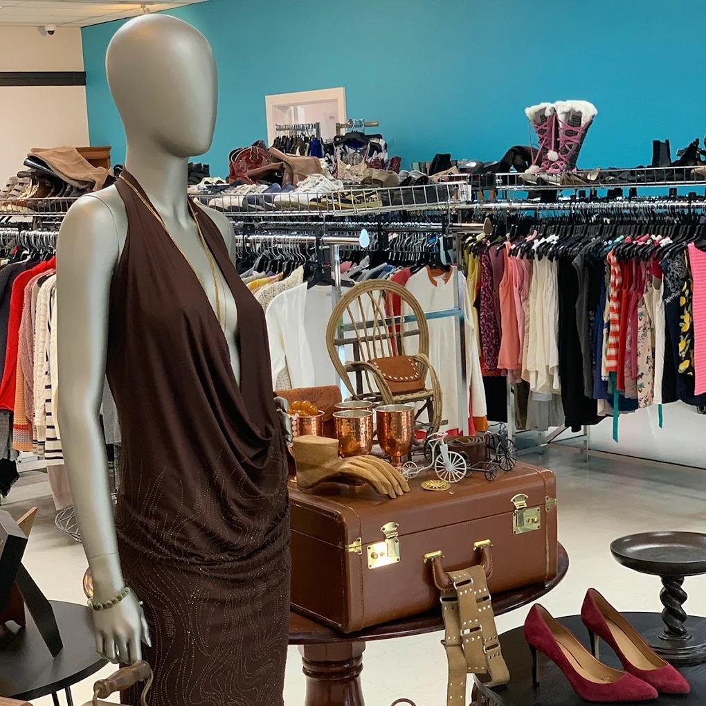 Mannequin in brown dress beside vintage luggage in a clothing store